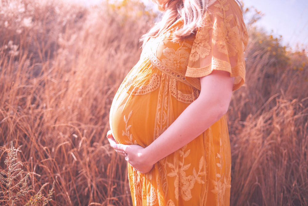 pregnant person in a field at sunset